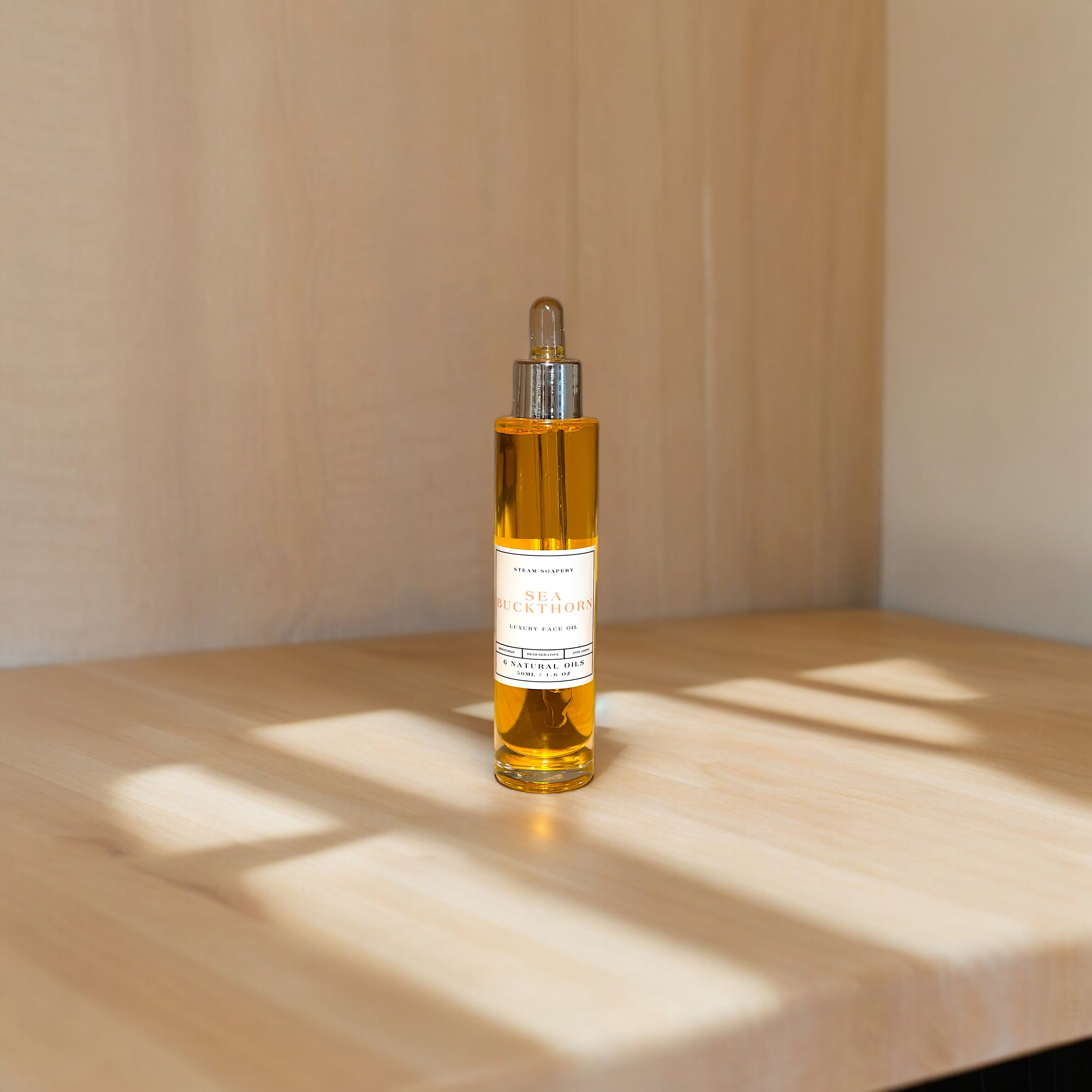 A tall, transparent bottle of Sea Buckthorn face oil with a golden-yellow liquid inside, placed on a wooden surface. The bottle features a label reading 'Sea Buckthorn Everyday Face Oil - 10 Natural Oils' and a dropper cap for dispensing the oil. Additional text on the image reads 'STEAM SOAPERY SEA BUCKTHORN LUXURY FACE OIL REGENERATING 6 NATURAL OILS 50ML. 6 OZ’